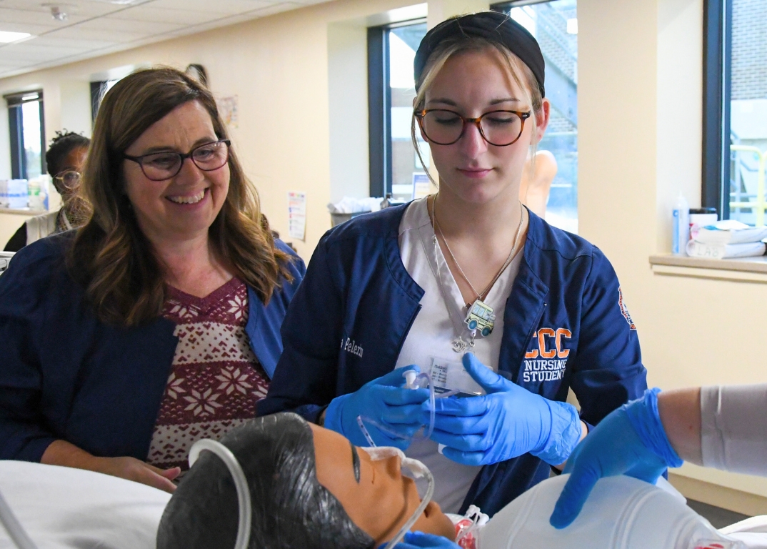 A nursing student working at a hospital bed with the instructor looking on